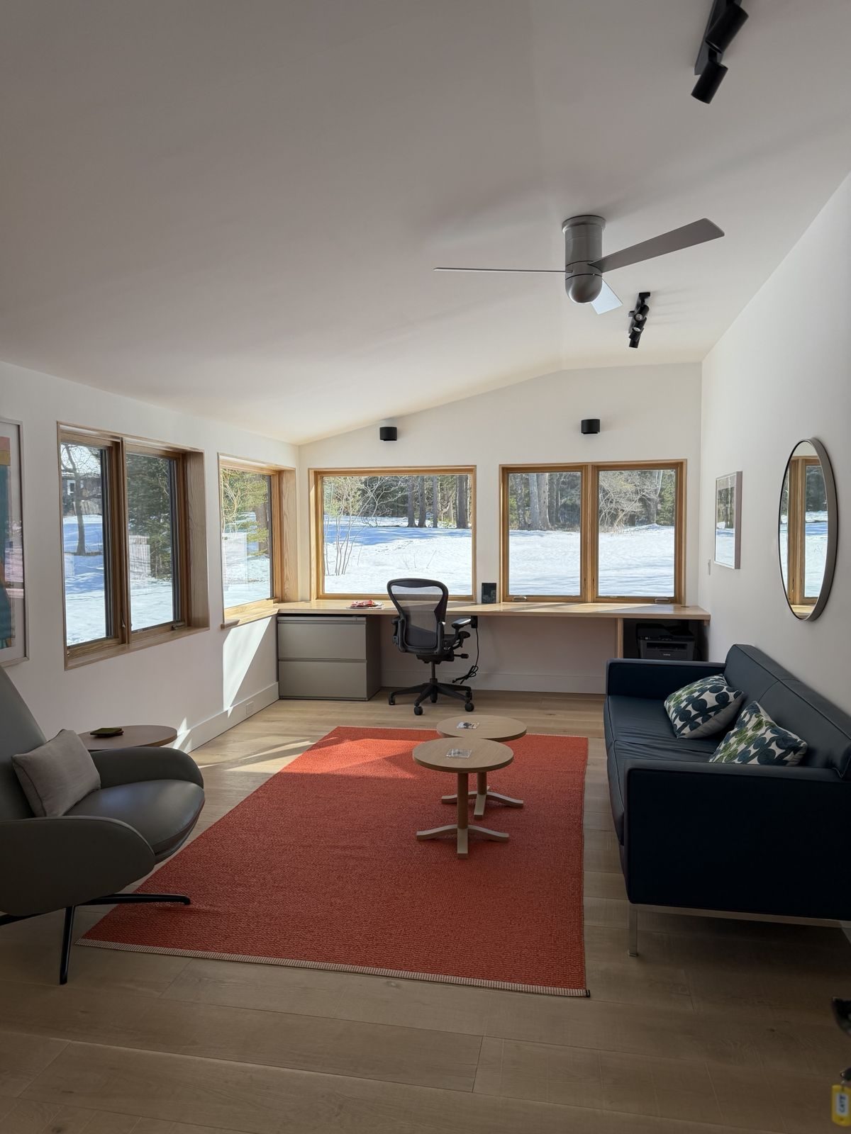 The Wreck Study: a desk along a wall of windows, orange rug and leather sofa