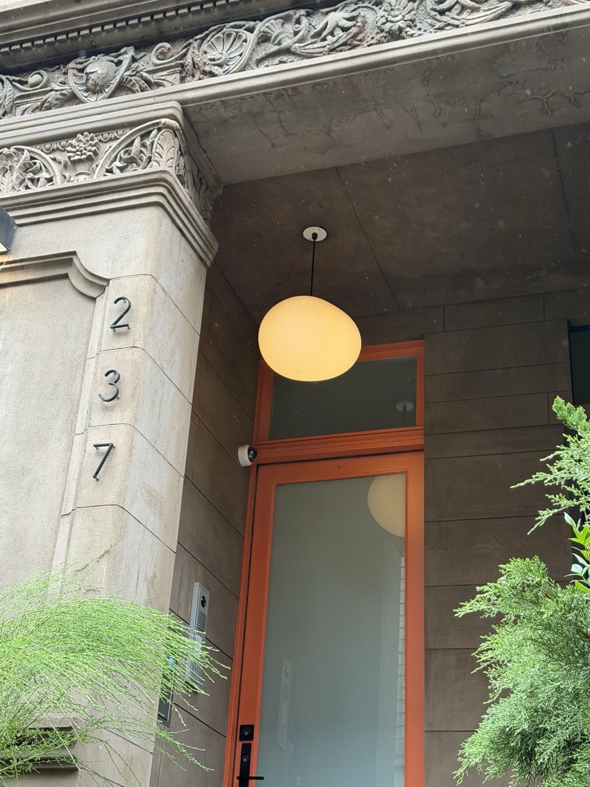 237 West 120th Street entry: carved brownstone surround, orange-framed glass door and a glowing pendant