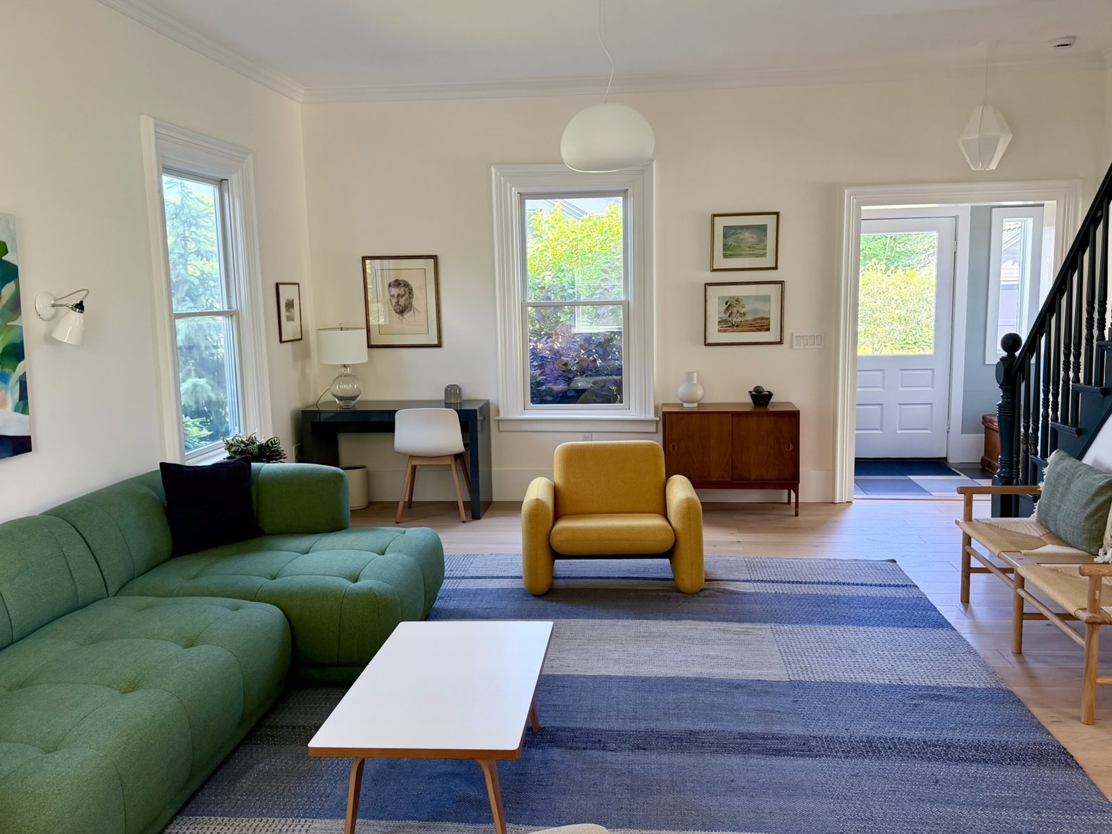 Living room: green sofa, yellow chair, blue rug and the front door beyond