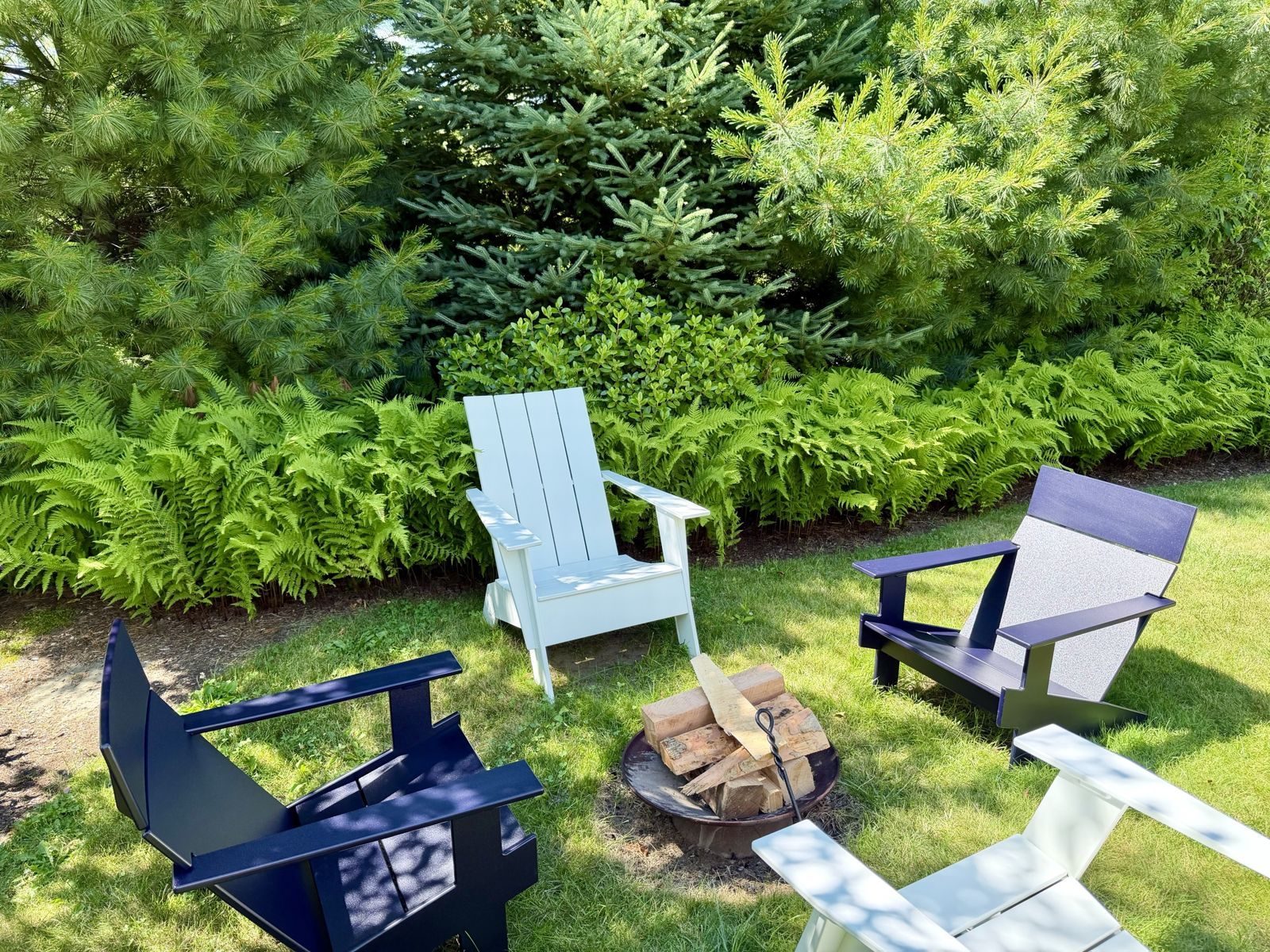 Adirondack chairs around a fire pit, ringed by ferns and pines