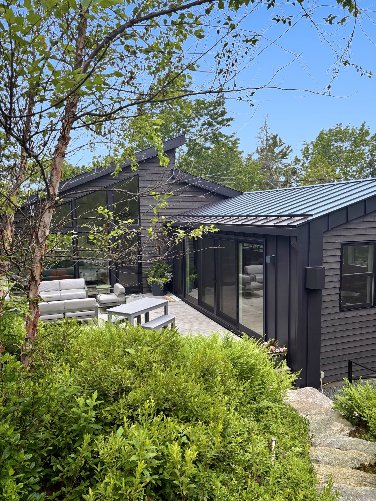 The Garage: black-shingled walls of glass and a shed roof above the deck, birches and ferns in front